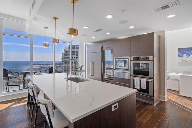 kitchen with built in appliances, decorative light fixtures, sink, and a kitchen island with sink