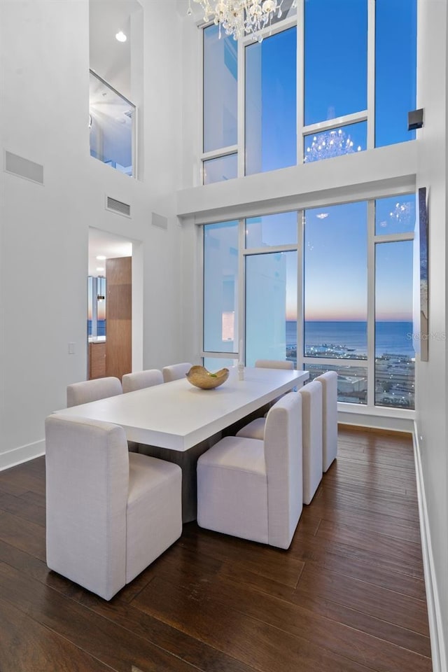 unfurnished dining area featuring a towering ceiling, an inviting chandelier, and dark wood-type flooring