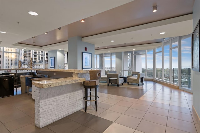 kitchen featuring light stone countertops, a wall of windows, a tray ceiling, a breakfast bar, and light tile patterned flooring