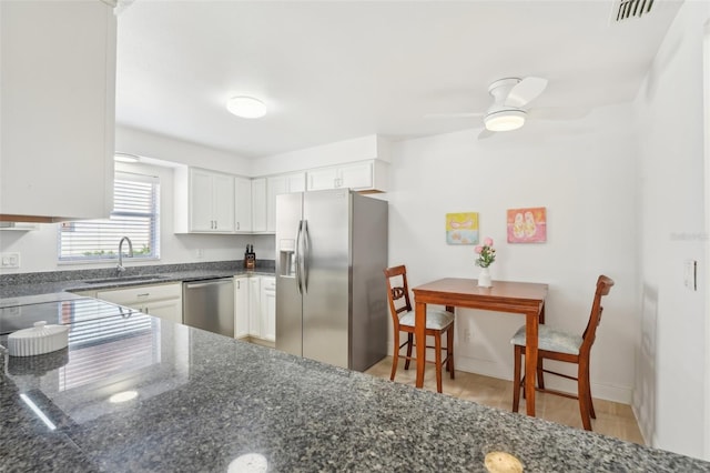 kitchen with sink, ceiling fan, dark stone countertops, appliances with stainless steel finishes, and white cabinetry