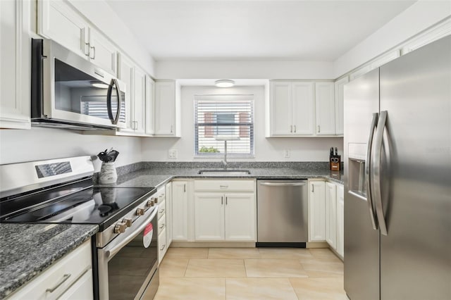 kitchen with white cabinets, sink, dark stone countertops, light tile patterned floors, and appliances with stainless steel finishes