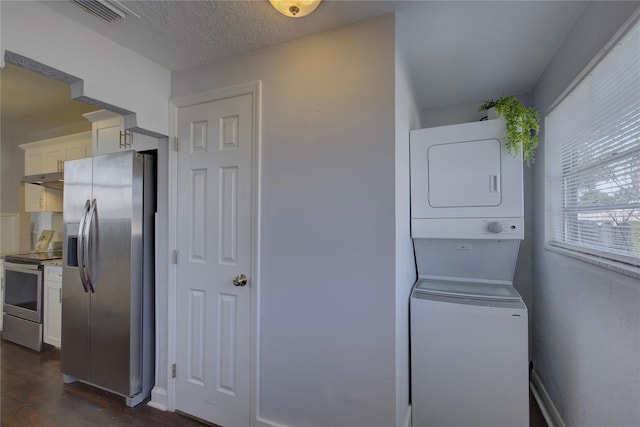 clothes washing area with dark wood-type flooring, stacked washing maching and dryer, and a textured ceiling