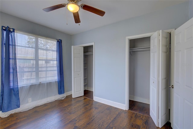 unfurnished bedroom with two closets, dark hardwood / wood-style floors, and ceiling fan