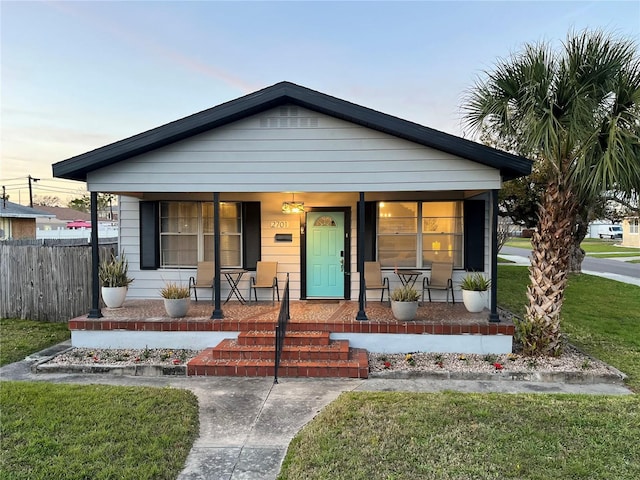 bungalow-style house with a porch, fence, and a front lawn