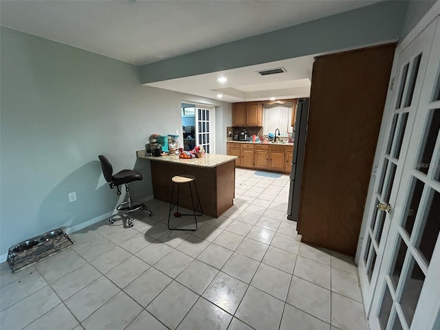 kitchen with kitchen peninsula, tasteful backsplash, sink, light tile patterned floors, and a breakfast bar area