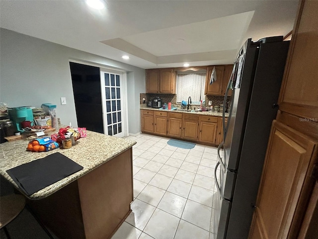 kitchen featuring light stone countertops, sink, tasteful backsplash, black fridge, and light tile patterned floors