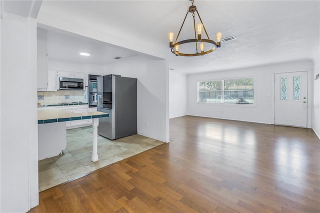 kitchen featuring an inviting chandelier, white cabinets, stainless steel refrigerator with ice dispenser, tasteful backsplash, and tile counters