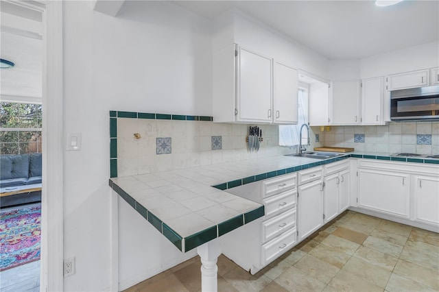 kitchen featuring gas cooktop, backsplash, sink, tile countertops, and white cabinets