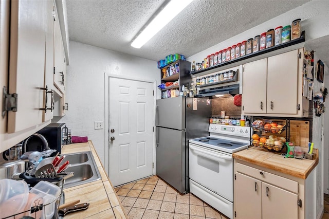 kitchen featuring white electric stove, stainless steel fridge, light tile patterned floors, a textured ceiling, and extractor fan