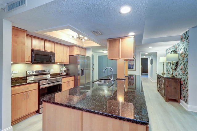 kitchen featuring appliances with stainless steel finishes, light brown cabinetry, a tray ceiling, light hardwood / wood-style flooring, and a chandelier