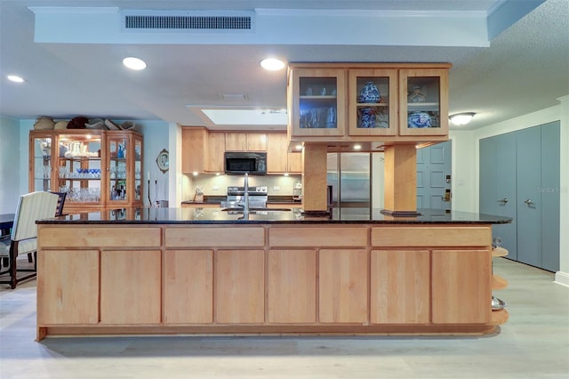 kitchen featuring appliances with stainless steel finishes, light brown cabinetry, a skylight, sink, and dark stone countertops