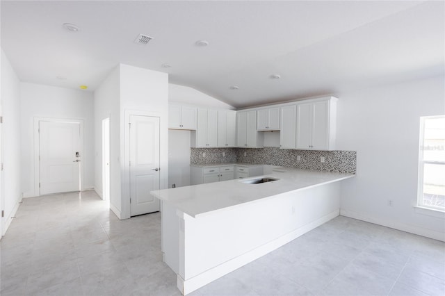 kitchen featuring white cabinets, tasteful backsplash, kitchen peninsula, and vaulted ceiling