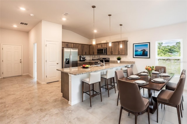 kitchen featuring a kitchen bar, appliances with stainless steel finishes, kitchen peninsula, light stone counters, and decorative light fixtures