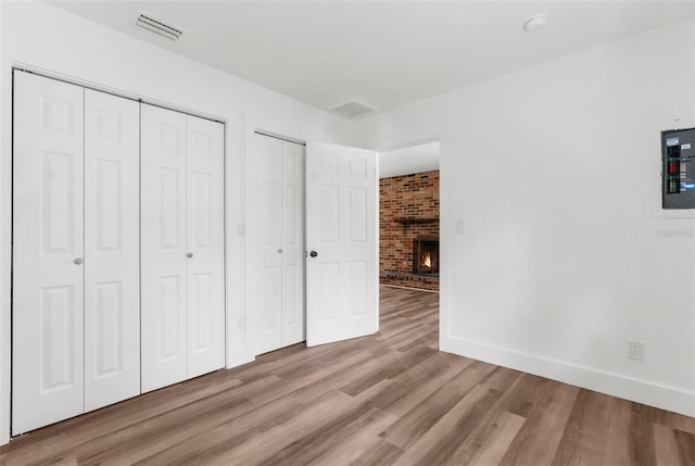 unfurnished bedroom with multiple closets, light wood-type flooring, brick wall, and a brick fireplace