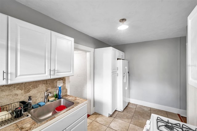 kitchen with stove, white refrigerator with ice dispenser, sink, light tile patterned floors, and white cabinetry