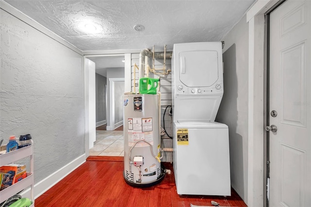 clothes washing area with gas water heater, stacked washing maching and dryer, and wood-type flooring