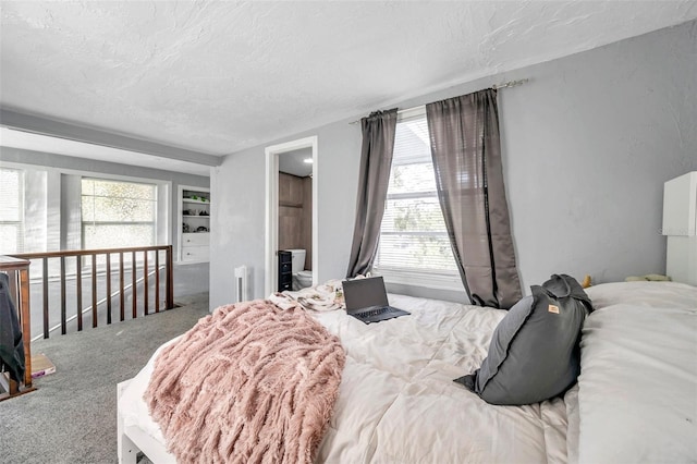 carpeted bedroom with multiple windows, ensuite bath, and a textured ceiling