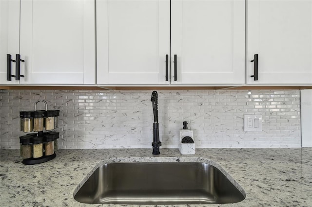 details with white cabinetry, sink, light stone counters, and tasteful backsplash