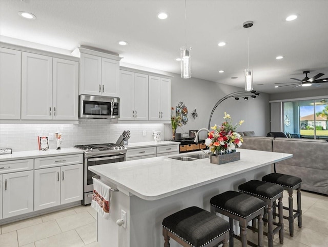 kitchen with sink, stainless steel appliances, decorative light fixtures, a breakfast bar area, and a kitchen island with sink