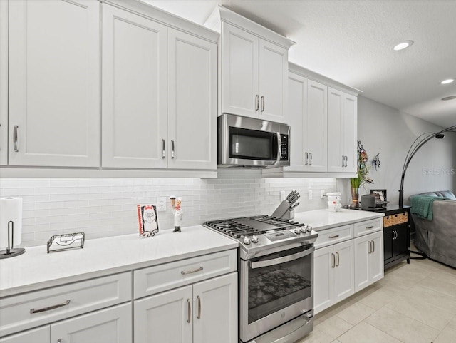 kitchen with appliances with stainless steel finishes, tasteful backsplash, a textured ceiling, light tile patterned floors, and white cabinetry