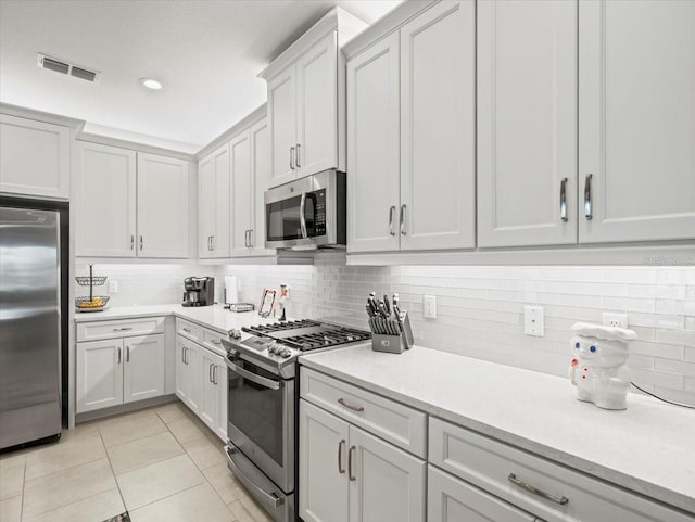 kitchen with decorative backsplash, white cabinets, stainless steel appliances, and light tile patterned floors