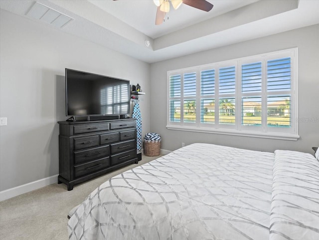 carpeted bedroom with a raised ceiling and ceiling fan