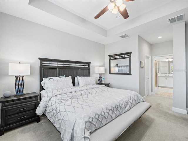 bedroom featuring light carpet, a tray ceiling, ceiling fan, and ensuite bathroom