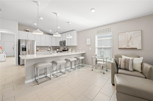 kitchen with vaulted ceiling, hanging light fixtures, appliances with stainless steel finishes, kitchen peninsula, and white cabinets