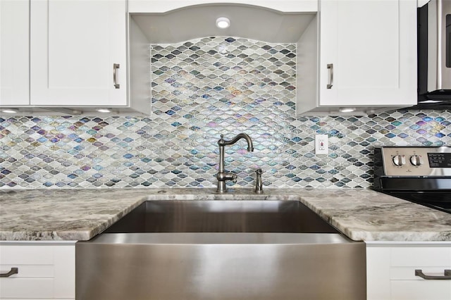 kitchen with white cabinetry, light stone counters, and sink