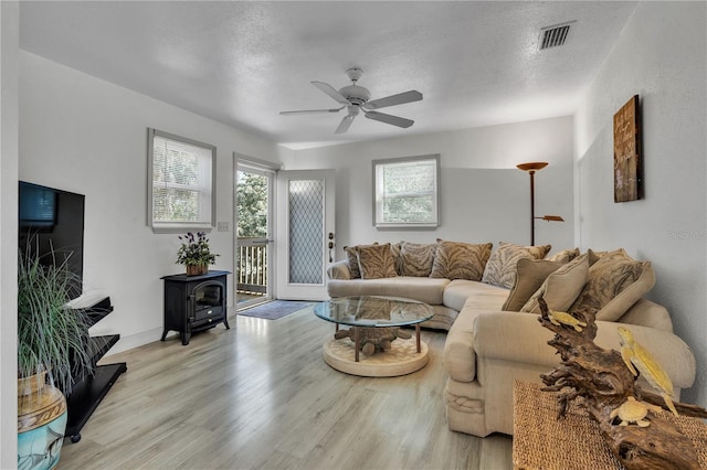 living room with ceiling fan, light wood-type flooring, a wood stove, and a textured ceiling