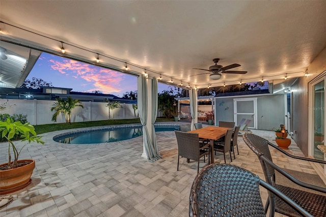 pool at dusk featuring ceiling fan and a patio area