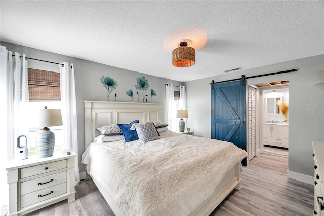 bedroom with a textured ceiling, ensuite bathroom, light hardwood / wood-style flooring, and a barn door