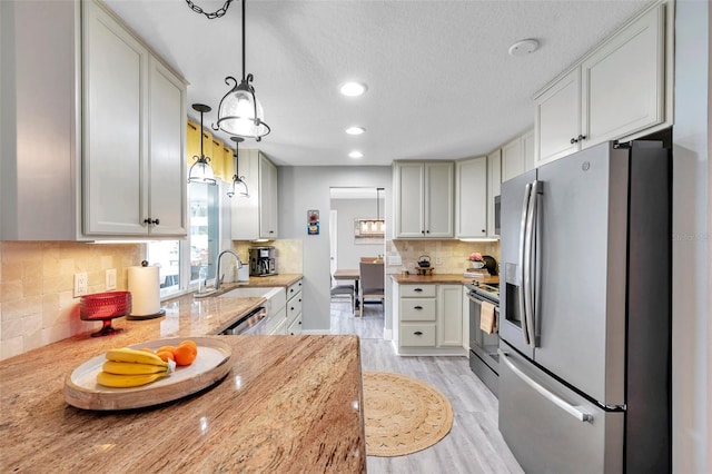 kitchen with light stone counters, pendant lighting, appliances with stainless steel finishes, and tasteful backsplash