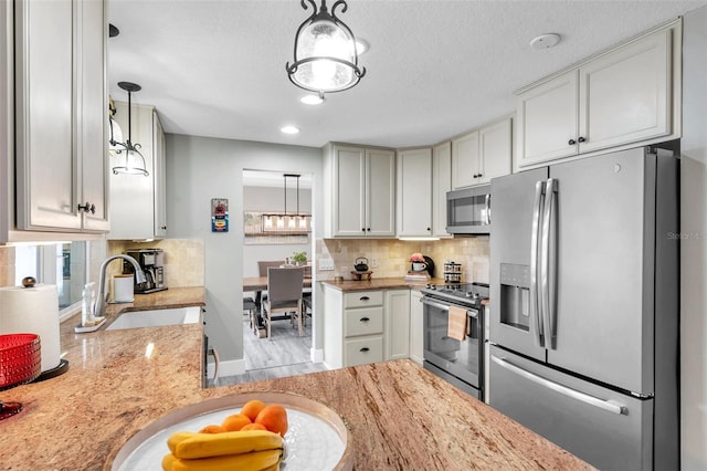 kitchen featuring stainless steel appliances, white cabinetry, hanging light fixtures, and sink