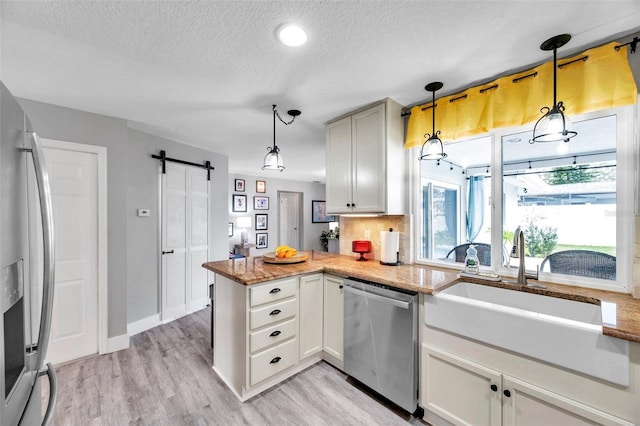 kitchen with appliances with stainless steel finishes, pendant lighting, a barn door, and backsplash