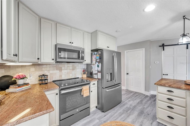 kitchen featuring white cabinetry, a barn door, stainless steel appliances, backsplash, and hanging light fixtures