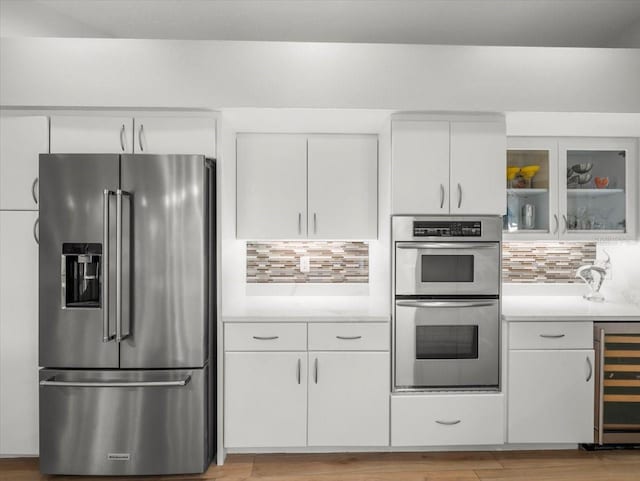 kitchen with tasteful backsplash, white cabinetry, beverage cooler, and appliances with stainless steel finishes