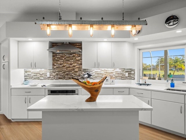 kitchen with oven, white cabinets, wall chimney exhaust hood, and hanging light fixtures