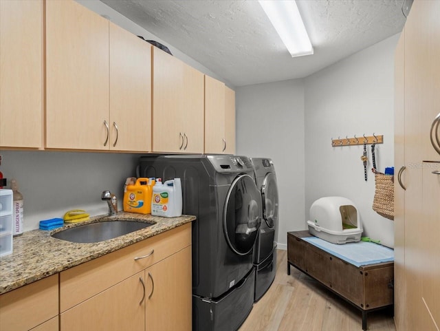 laundry area with cabinets, a textured ceiling, sink, washer and dryer, and light hardwood / wood-style floors