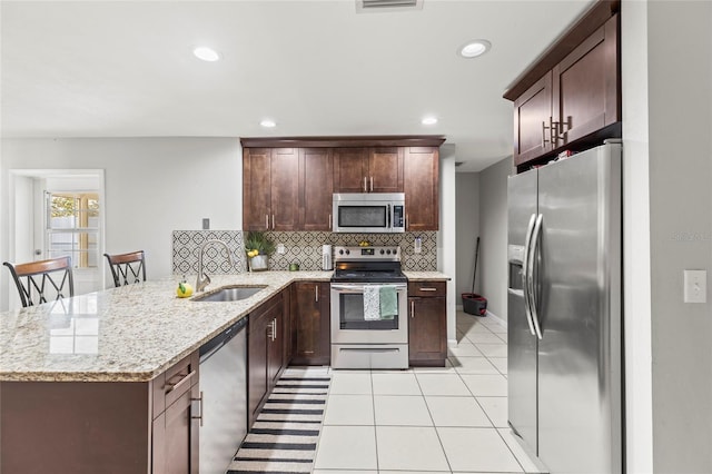 kitchen with kitchen peninsula, tasteful backsplash, light stone counters, stainless steel appliances, and sink