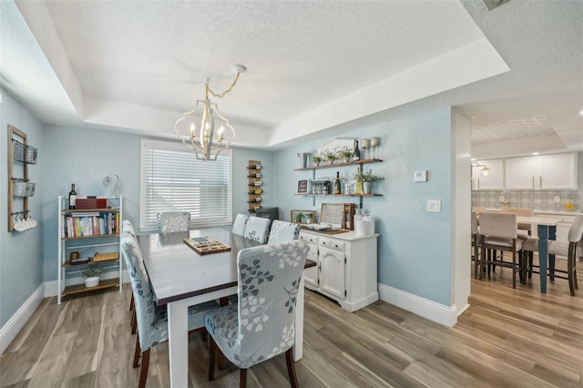 13945 75th Ave, Seminole, FL 33776 - dining space featuring a raised ceiling, a chandelier, a textured ceiling, light wood-style flooring, and baseboards