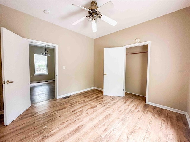 unfurnished bedroom with ceiling fan with notable chandelier, visible vents, wood finished floors, lofted ceiling, and baseboards