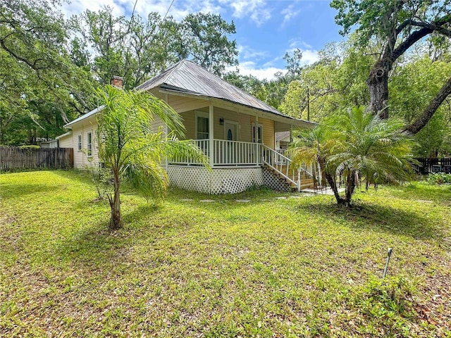 view of front of house featuring a chimney, a front lawn, metal roof, fence, and covered porch