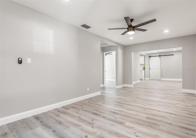 unfurnished room with ceiling fan, a barn door, and light hardwood / wood-style flooring