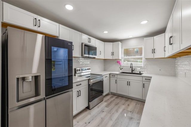 kitchen featuring white cabinetry, sink, backsplash, stainless steel appliances, and light hardwood / wood-style flooring