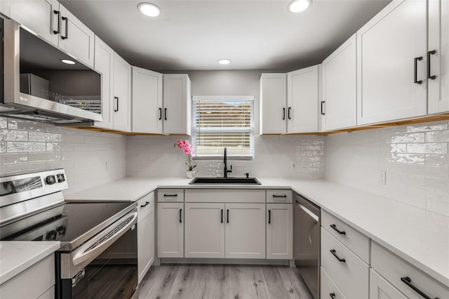 kitchen with sink, tasteful backsplash, light wood-type flooring, stainless steel appliances, and white cabinets