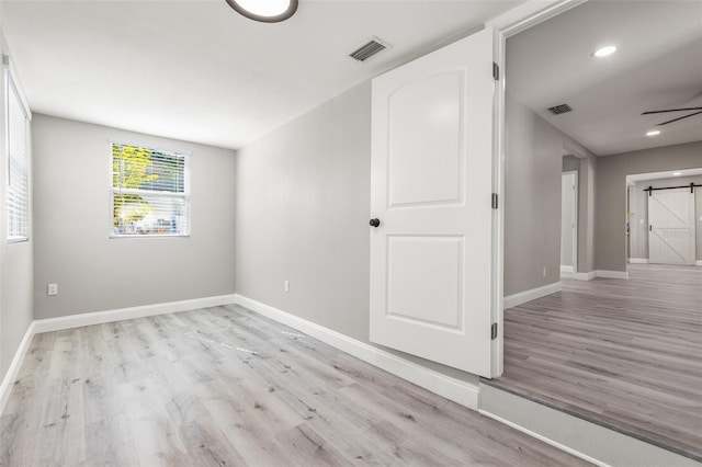 unfurnished room with light hardwood / wood-style flooring and a barn door