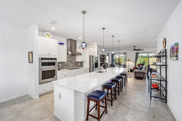 kitchen with sink, hanging light fixtures, wall chimney range hood, a kitchen bar, and a center island with sink