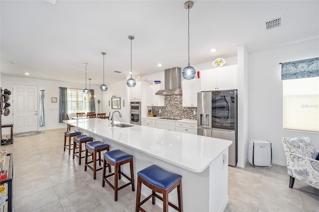 kitchen with wall chimney exhaust hood, sink, decorative light fixtures, a breakfast bar area, and a large island