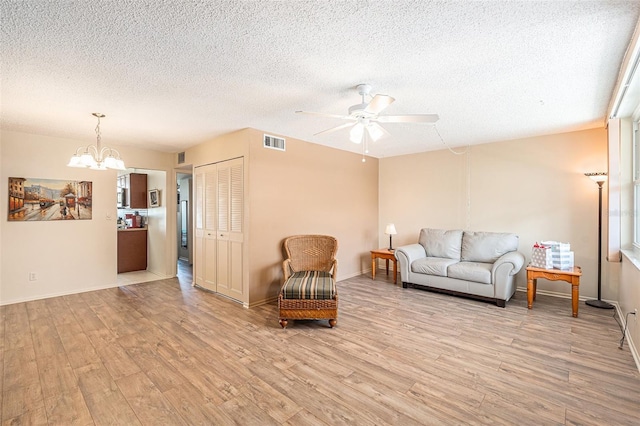 living room with a textured ceiling, ceiling fan with notable chandelier, and light hardwood / wood-style floors